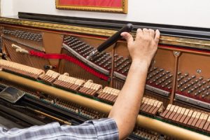 Closeup on hand tuning an upright piano using lever and tools